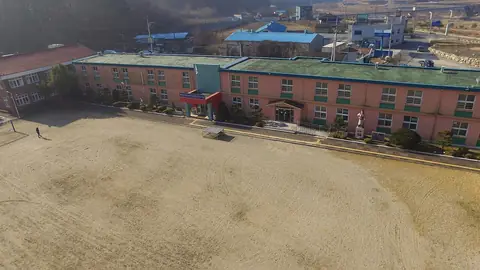 하늘에서 내려다본 2층짜리 분홍색 학교 건물과 넓은 흙 운동장