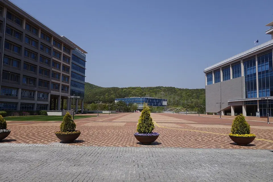 넓은 벽돌 광장 양옆으로 유리창이 많은 건물이 서 있고 멀리 산이 보이는 UNIST 캠퍼스