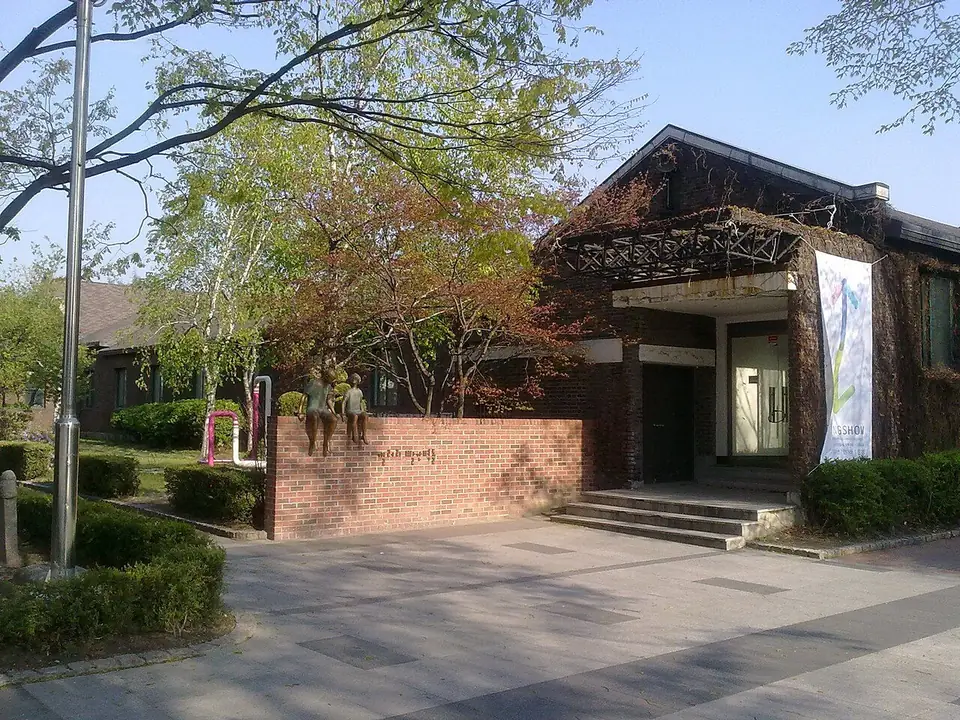 나무 사이에 있는 붉은 벽돌과 짙은 색 지붕의 낮은 옛 건물과 앞마당