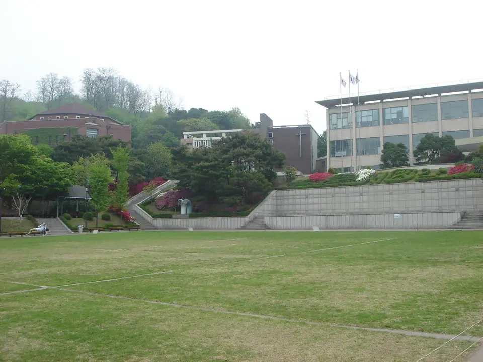 넓은 잔디 운동장 너머로 보이는 서강대학교 건물들과 꽃이 핀 언덕