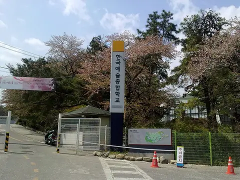 벚꽃 핀 나무 사이로 ‘한국예술종합학교’ 세로 교명 기둥과 교문, 캠퍼스 안내도가 보이는 모습