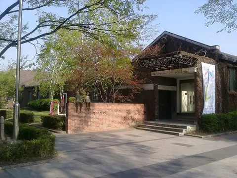 나무 사이에 있는 붉은 벽돌과 짙은 색 지붕의 낮은 옛 건물과 앞마당